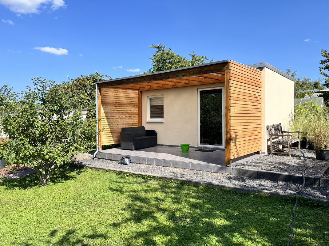 Gartenhaus mit Holzverkleidung und integrierter Terrassenüberdachung im Sommer.